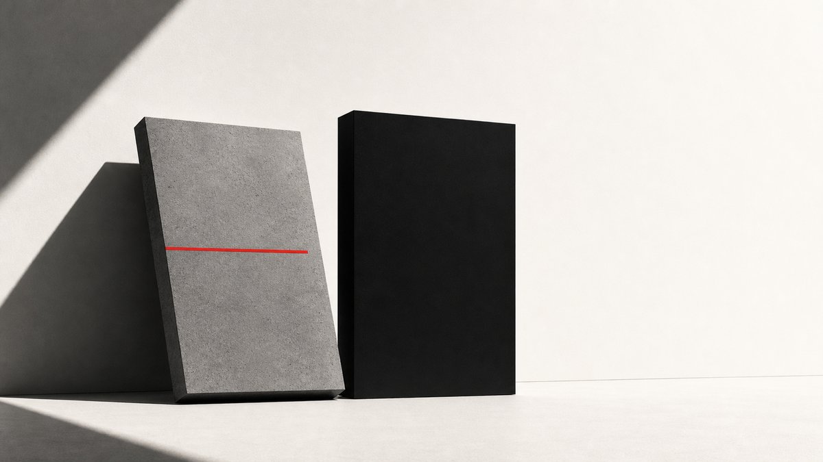 Two sculptural monoliths against an off-white ground: a grey concrete slab tilted forward in soft shadow, beside a black upright slab; a thin horizontal red line bisects them.